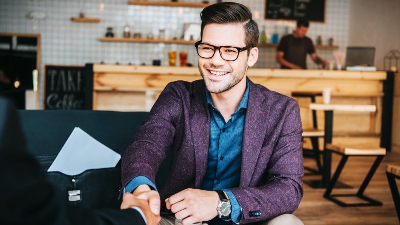 Attractive Business Man with Glasses and Wearing a Suit Shaking Hands in Cafe