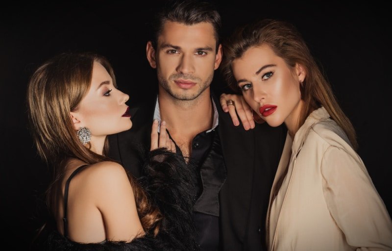 Attractive man with two beautiful women on black background