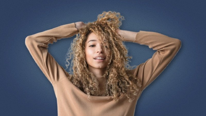 Attractive woman playing with her curly hair on blue background 1