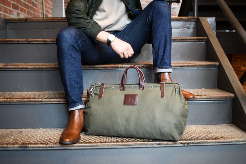 Bespoke Post Weekender Bag Outside Sitting At Feet of Model on Stairs Wearing Jeans and Boots Close Up