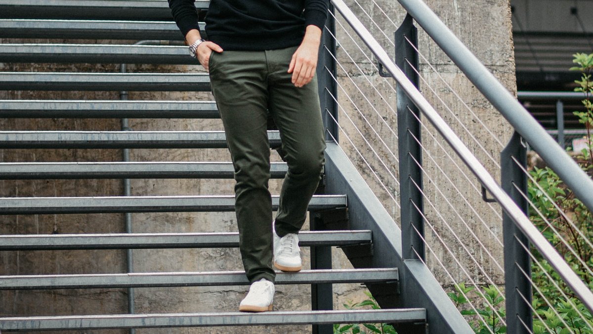 Best Chinos for Men Model Wearing Olive Asket Chinos Walking Down Stairs in White Sneakers