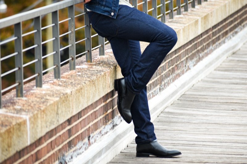 Best Jeans for Men Model Outside Leaning Against Guard Rail Wearing Slim Fit Dark Wash Jeans and Black Boots