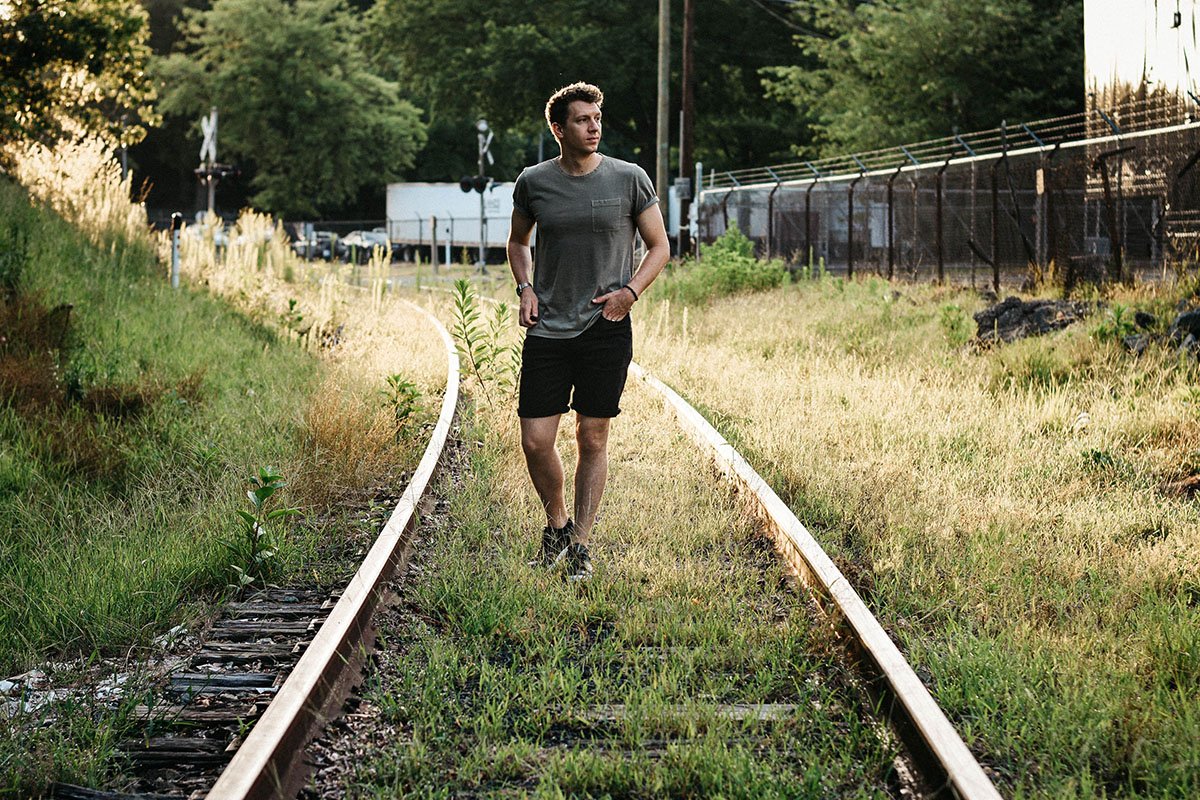 best mens shorts model standing on train tracks wearing duer performance denim jeans no sweat shorts