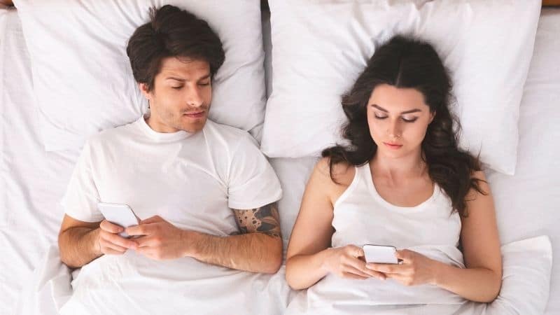 Couple in bed on phones with guy suspicious of girl