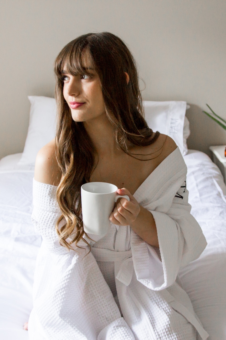 Female model wearing Luxor Linens Lakeview Signature Egyptian Cotton Spa Robe while holding a coffee and looking into the distance