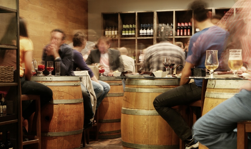 Hazy view of a drinking area with people sitting on barrels and drinking alcohol