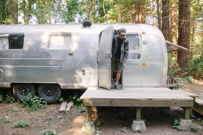 Man coming out of Airstream camper in the woods while wearing Carhartt Odessa Cap Force Delmont Tee Shoreline Jacket and Rugged Flex Cargo Shorts