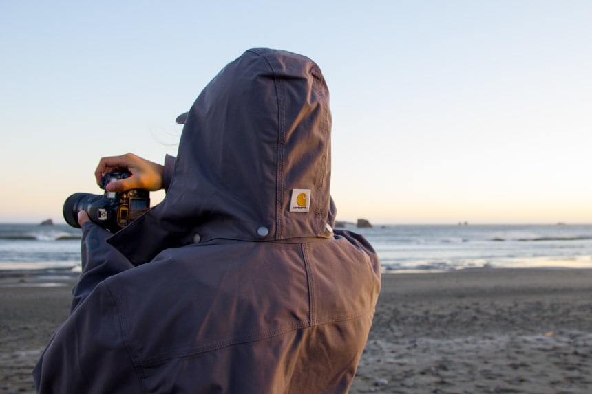 Man-holding-camera-and-taking-photos-while-wearing-Carhartt-Shoreline-Jacket-at-the-ocean wider shot