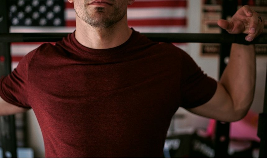 Man in maroon shirt holding barbell on his shoulders