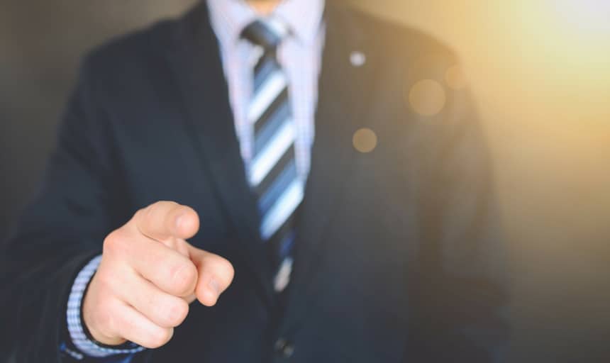 Man in suit and tie pointing at camera with sun glare in background