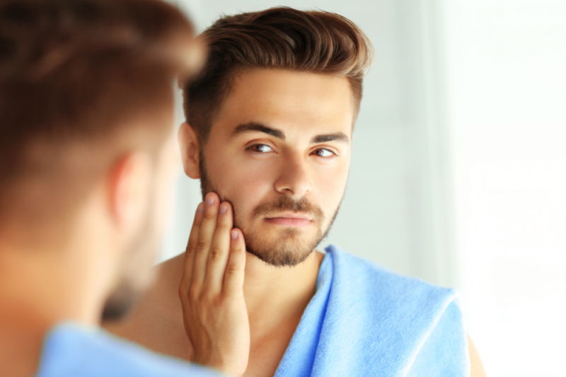 man looking into mirror at facial skin