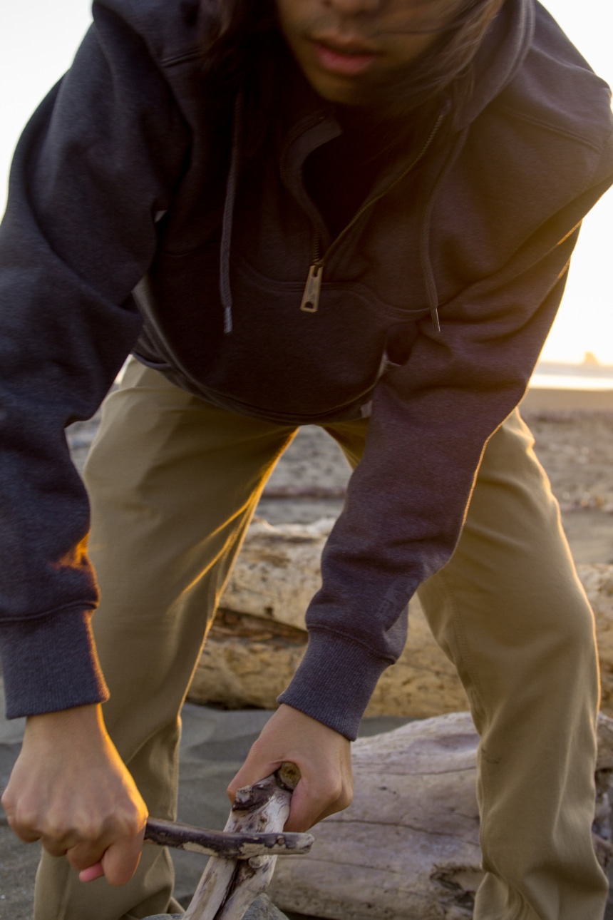 Man on beach trying to start fire with driftwood while wearing Carhartt Shoreline Jacket and Rugged Flex Rigby Dungaree