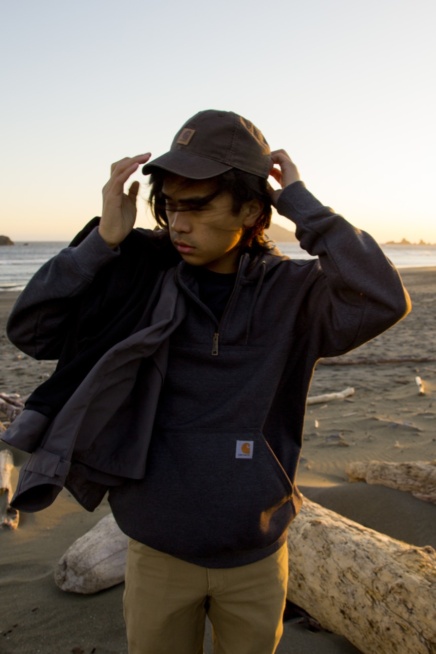 Man on beach wearing Carhartt Odessa Cap Rugged Flex Rigby Dungaree and Rain Defender Paxton Zip Mock Sweatshirt