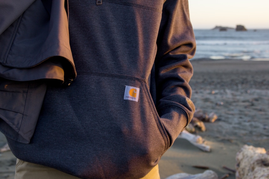 Man on beach wearing Carhartt Rain Defender Paxton Zip Mock Sweatshiert focusing on front pocket