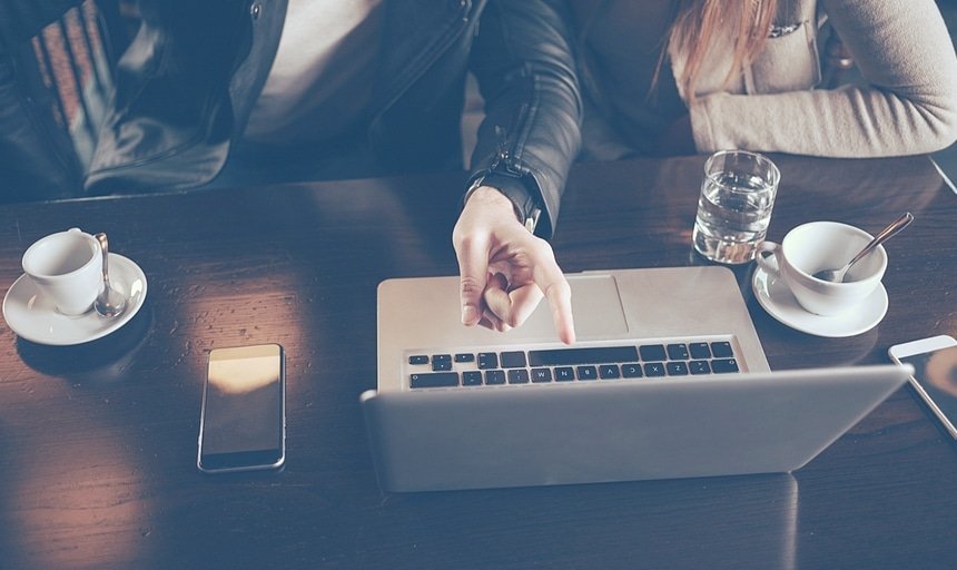 Man pointing at laptop screen while talking to girl at coffee shop