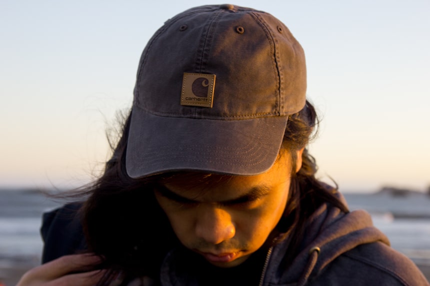 Man with long hair on a beach wearing Carhartt Odessa Cap b