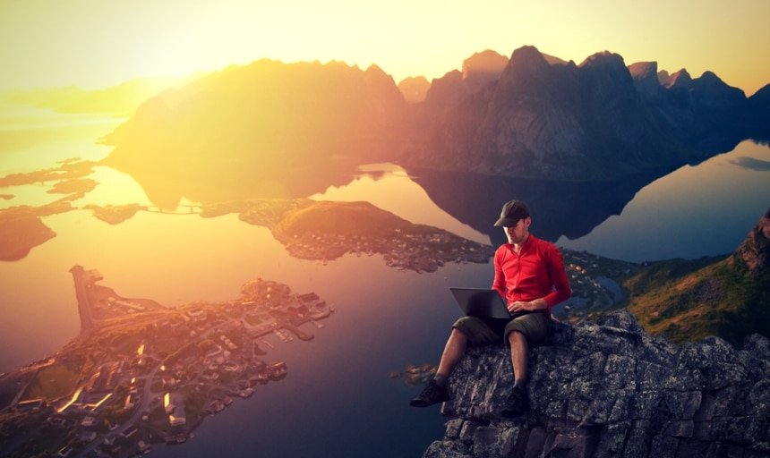 Man working on laptop on cliff with view 