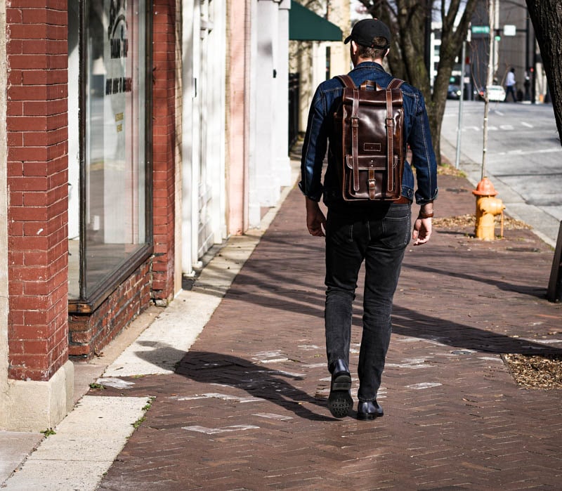 medium shot model wearing leather roll top backpack walking down sidewalk