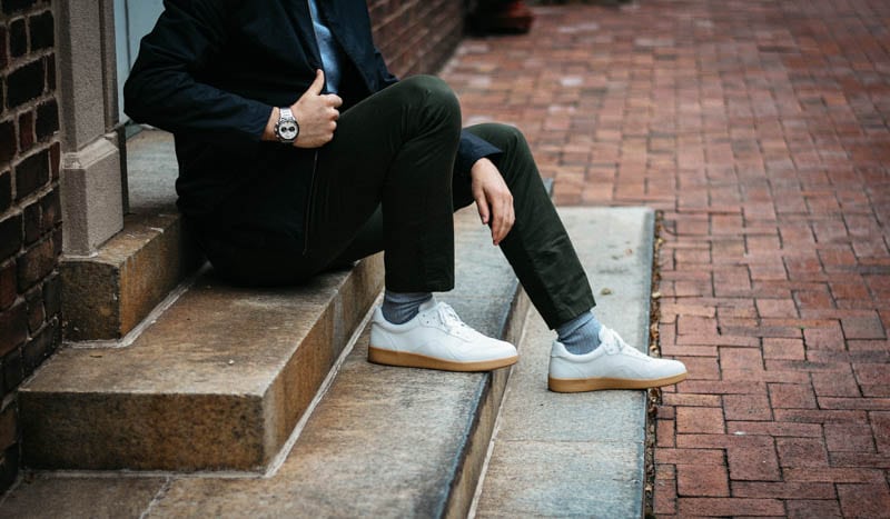 model adjusting black asket zip coat wearing olive asket chino everlane white tread sneaker and vincero apex racing watch