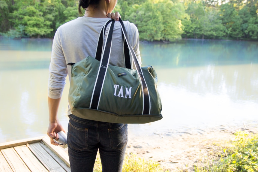 Model Holding Paravel Fold-Up Bagin Safari Green Over Shoulder Outside Near the Water