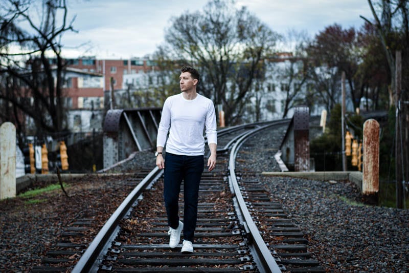 model in white rag and bone long sleeve shirt walking along train tracks
