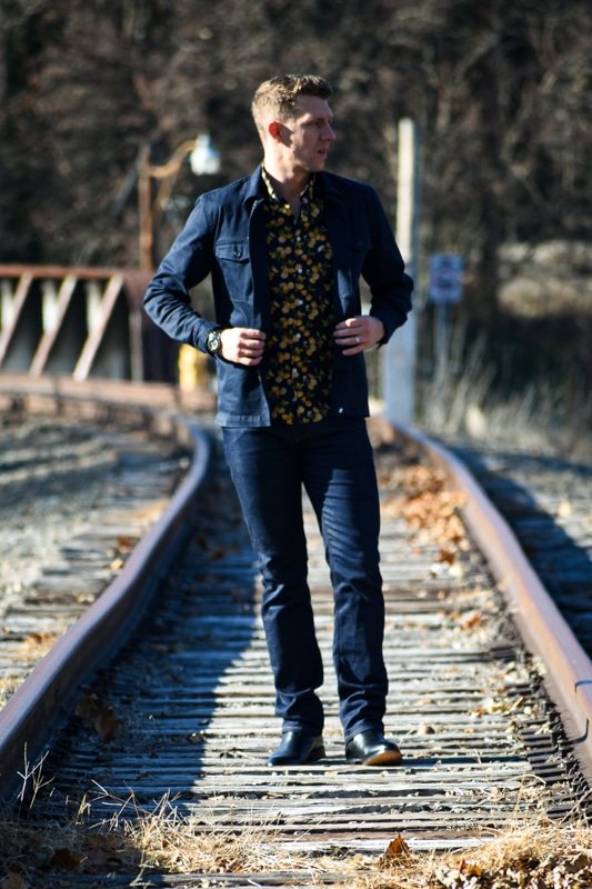 model on train tracks wearing navy and black outfit with dark blue jeans