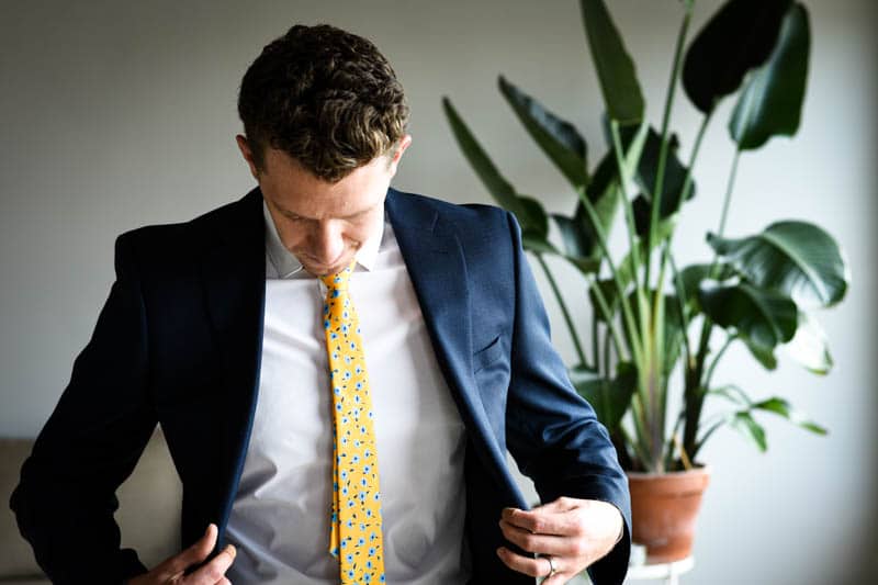 model opening blue suit jacket with white shirt and yellow tie