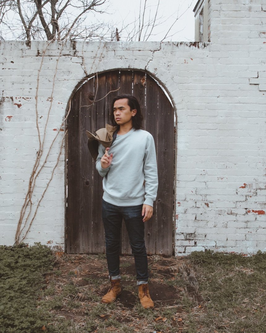 Model posing ooutside of a door wearing Everlane's men's range and holding midweight canvas jacket with one hand