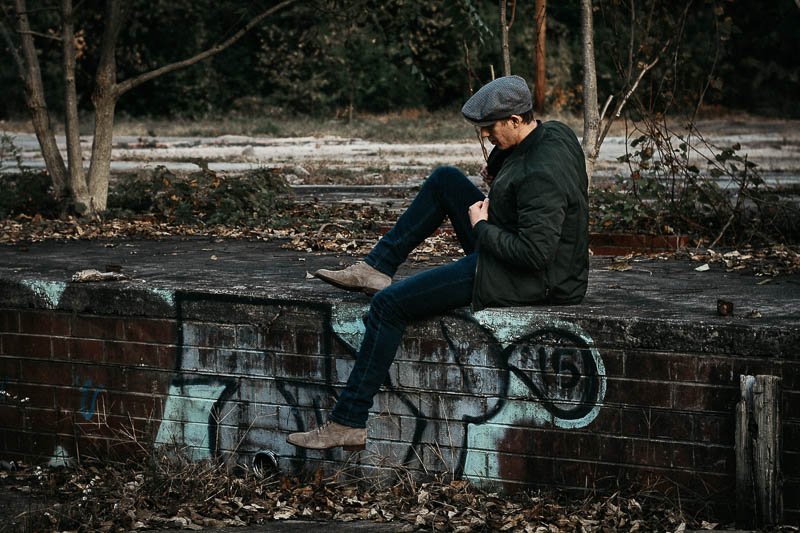 model sitting on wall in green frank and oak bomber jacket and hat