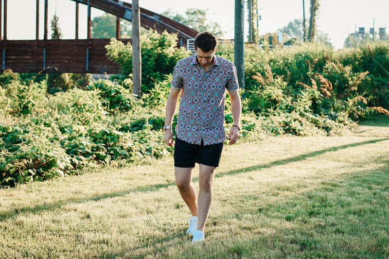 model walking toward camera in grass wearing robert graham shorts shirt and white minimalist sneakers