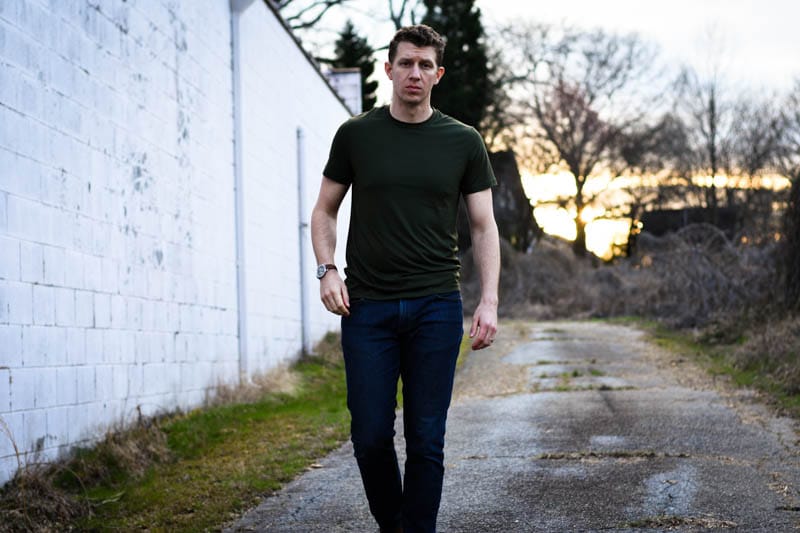 model wearing green tshirt and jeans walking against white wall