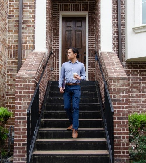 Model Wearing Mizzen+Main Beckett Dress Shirt While Walking Out of a House and holding coffee and a folder