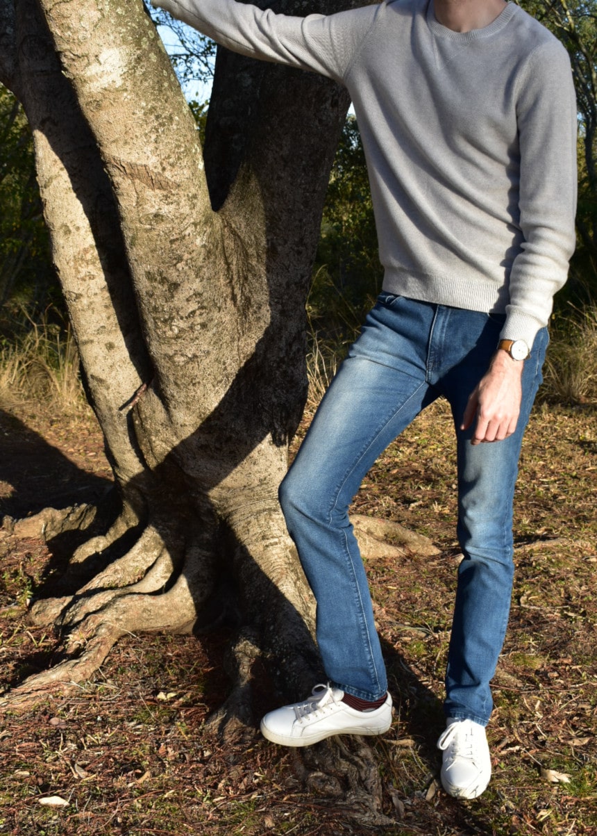 Model Wearing Mott & Bow Slim Laight Jeans with Liam Sweater Standing Up and Leaning On Tree with White Sneakers