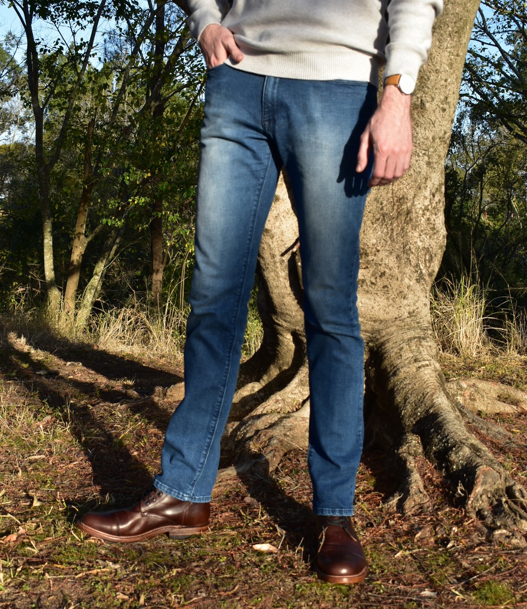 Model Wearing Mott & Bow Slim Laight Jeans with Liam Sweater Standing Up and Standing Next to Tree With Hand in Pocket and with White Sneakers - Torso Shot