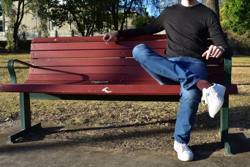 Model Wearing Mott & Bow Slim Laight Jeans with Slim Crew Long Sleeve Driggs Tee in Black, with Legs Crossed on Bench - Right Aligned