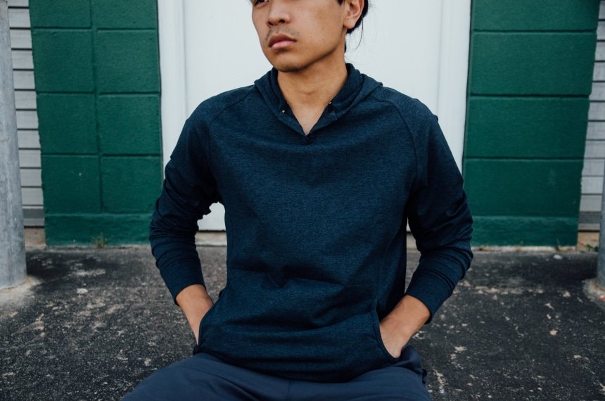 Model Wearing Public Rec Politan Hoodie And Sitting Down With Hands In Pockets