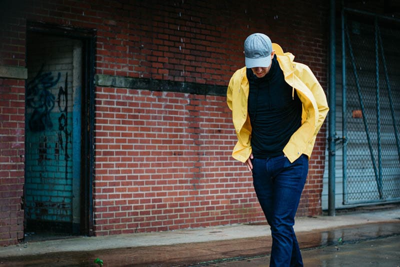 model wearing rains yellow waterproof jacket and everlane hat in the rain