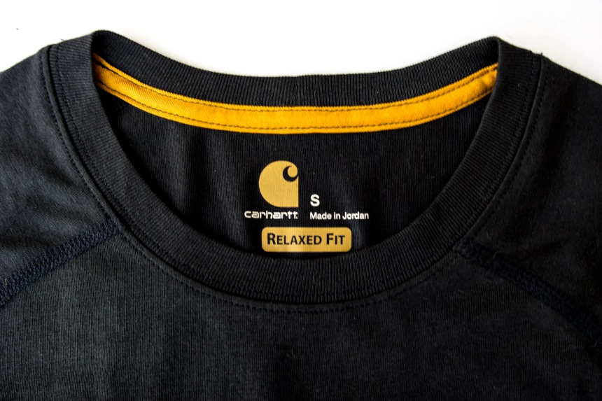 Neck of Carhartt Force Delmont Tee in navy front facing with yellow stitching and size small tag against white background