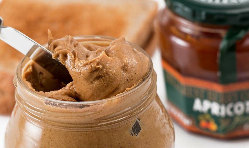 Peanut butter with knife in it with jam in background