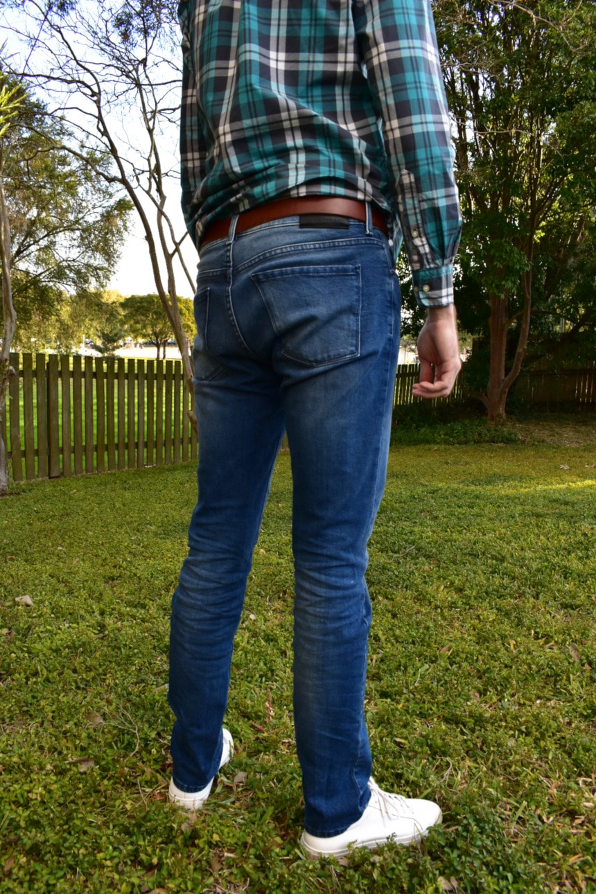 Picture of Model Wearing Mott & Bow Laight Jeans and a Flannel Shirt and White Sneakers While Standing in a Backyard