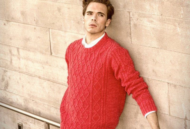 Shetland Sweaters Model Leaning Against the Wall Wearing a Red Sweater