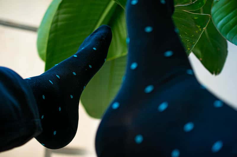 teal and navy polka dot sock against green leaf background