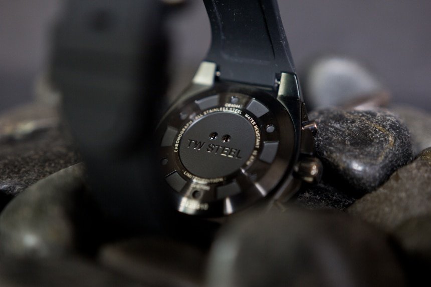 TW Steel CEO Tech watch back facing with logo propped on top of black stones on black background c