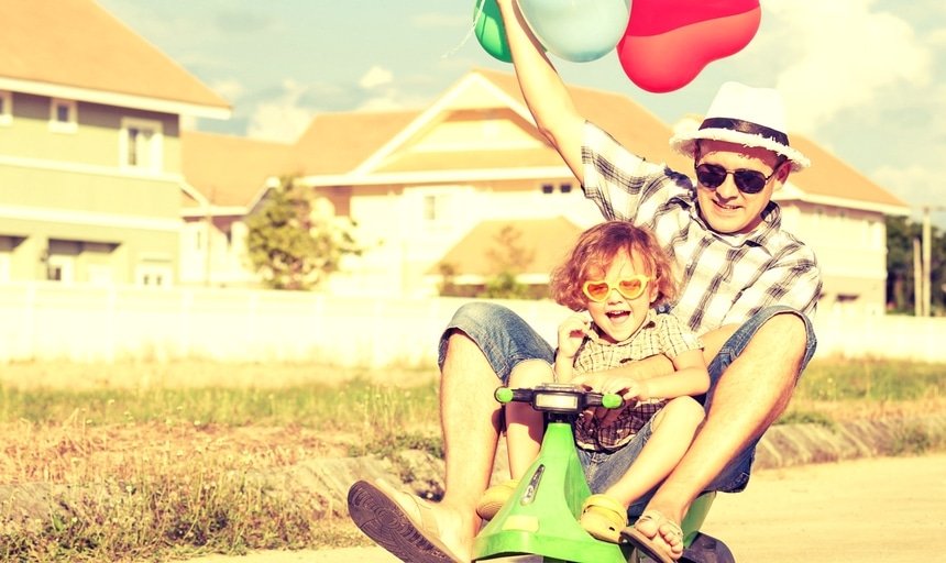 Uncle playing with nephew on toy bike holding balloons