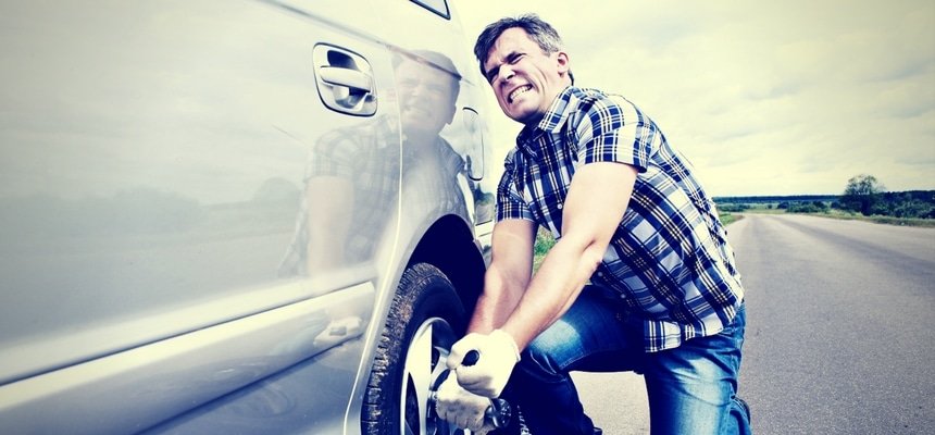 Man struggling to change tire of car